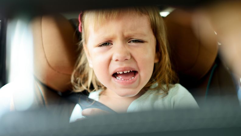 Lapsi vihaisena auton takapenkillä.